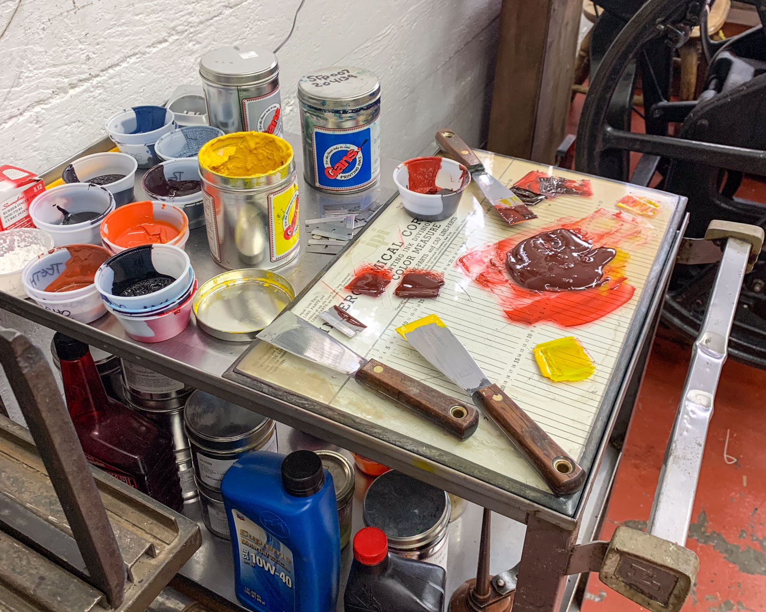 A glass table covered in piles of custom-mixed red and yellow letterpress ink. Tubs of other colors of ink sit on the back of the table.