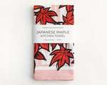 A folded kitchen towel featuring a red and black illustration of Japanese maple leaves. A white belly band reads 'Lauren Nishizaki Designs; Japanese maple kitchen towel; 100% cotton; 27x27