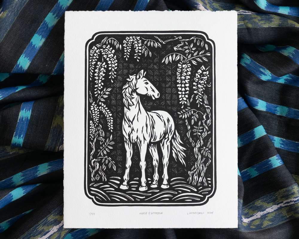 Black and white illustration of a horse under wisteria vines. The white paper sits on top of rumpled blue striped fabric.