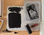 A grey carved linoleum block on a bamboo table with a glass inking plate covered in black ink. The linoleum block is partially covered in black ink.