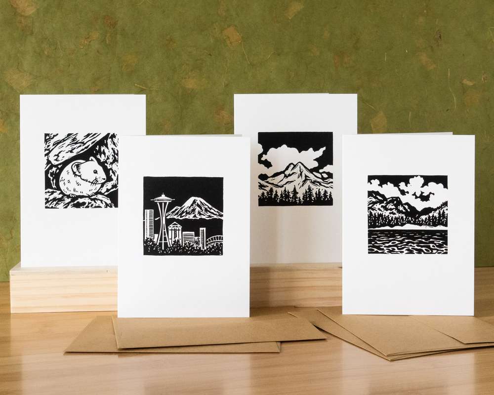 4 black and white cards on a wood platform with brown envelopes in the foreground